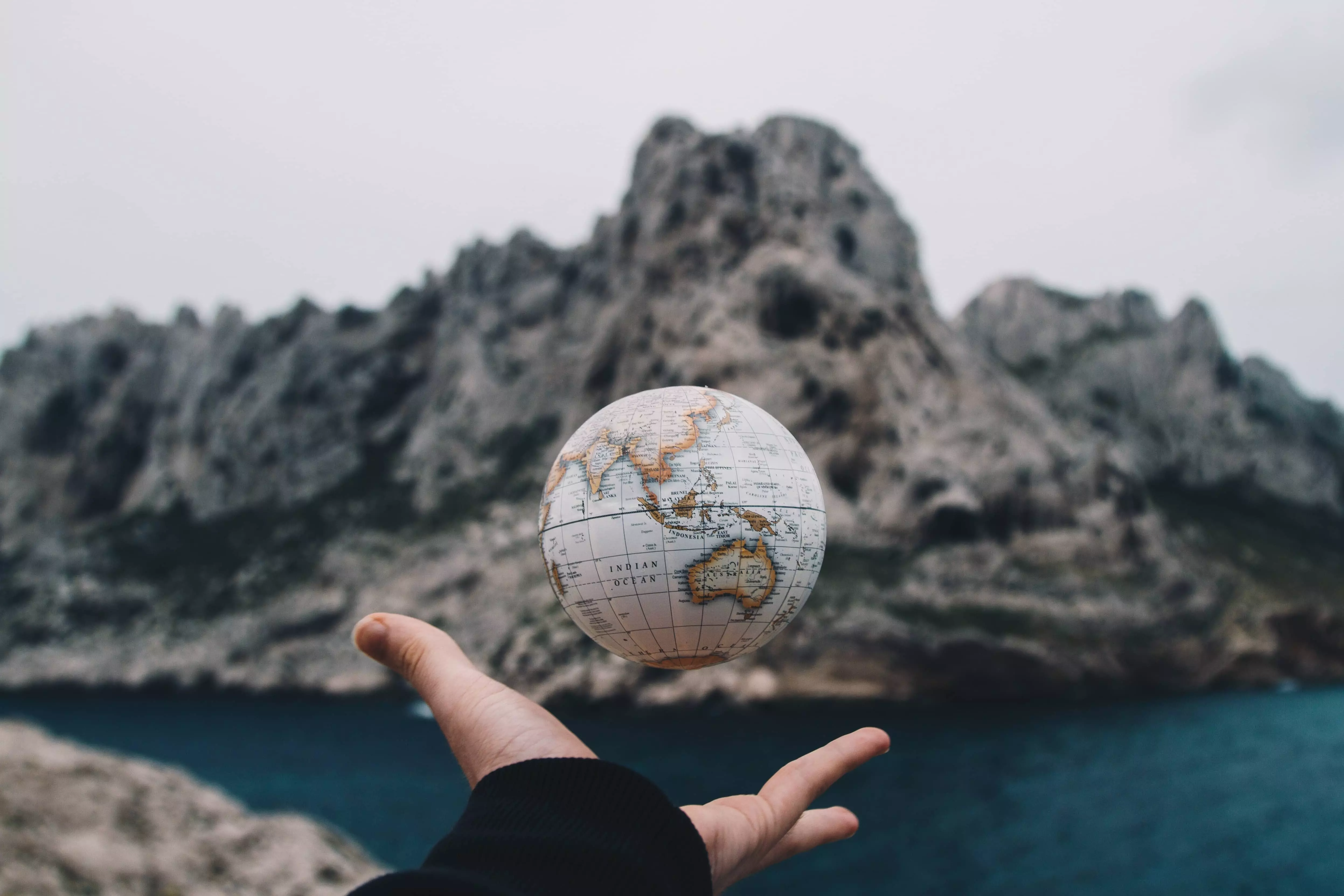 Hand mit hochgeworfenem kleinen Ball mit alter Weltkarte vor steiniger Felswand