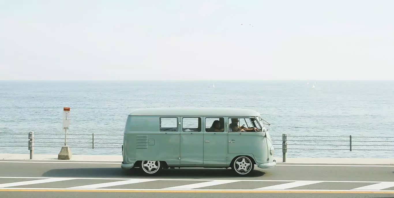 Reisen mit Auto - Foto eines VW Bullies fahrend entlang einer Meerespromenadenstraße